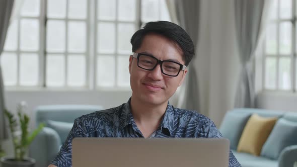 Asian Man Video Call On Laptop And Writing On Notebook At Home