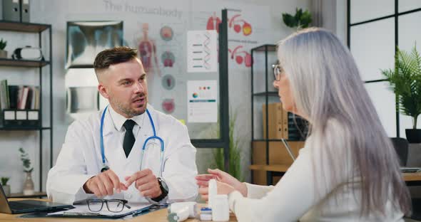 Physician in Medical Coat Sitting at Table Consulting Middle Aged Female Patient