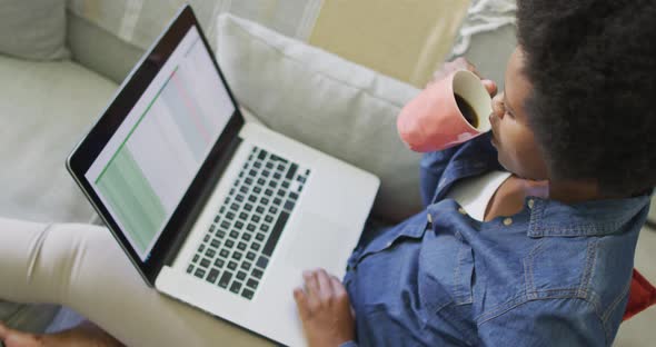 Happy african american woman sitting on sofa, using laptop