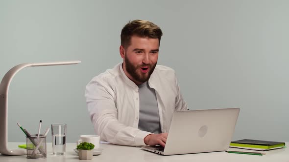 Young Man Typing on Computer Browsing Web Looking at Screen with Enthusiastic Wow Expression on His