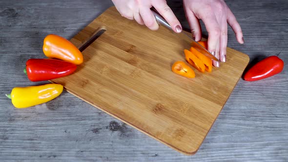 A woman in a kitchen cutting up orange and red peppers on a wooden chopping board