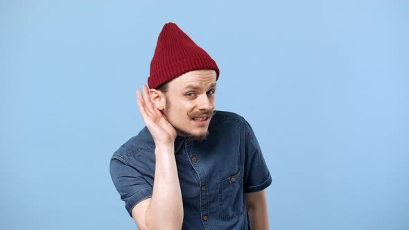 Portrait of Cool Hipster Man 20s Wearing Hat and Denim Shirt Holding Hand at Ear and Asking Again As