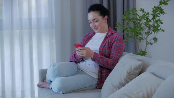 Woman Typing on Phone Sitting on Sofa at Home, Businesswoman Sits at Home Types on Smartphone Checks