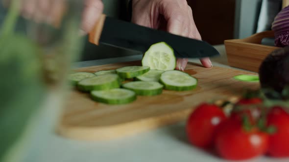 Closeup of Female Hands Slicing Cucumber with Knife in Kitchen While Housewife Cooking Salad From