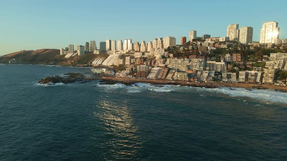 Aerial view flying across Reñaca sunny cityscape beach coastline reflecting in ocean