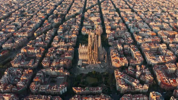 Rising drone shot of La Sagrada Familia Basilica surrounded by square grid houses Barcelona at sunri