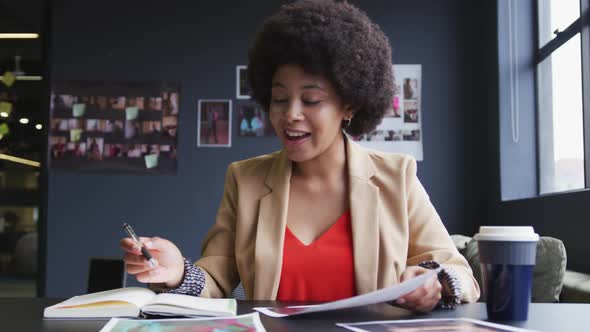 Mixed race businesswoman sitting having a video chat going through paperwork in a modern office