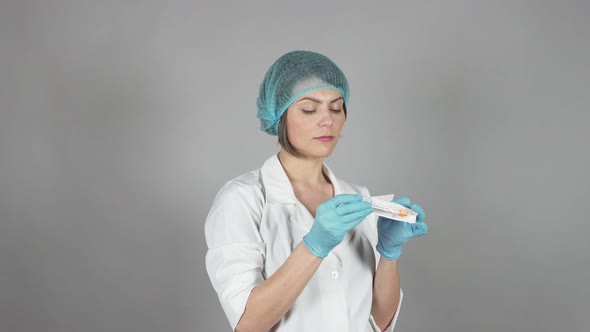 Young Female Doctor in Gloves Holding a Syringe Isolated on Grey Background