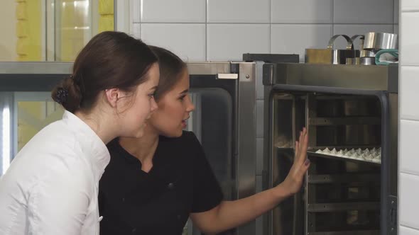 Beautiful Female Confectioner and Her Assistant Examining Merengues in the Oven