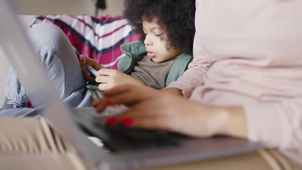 Mixed Race Boy Plays on the Phone While His Mom Works