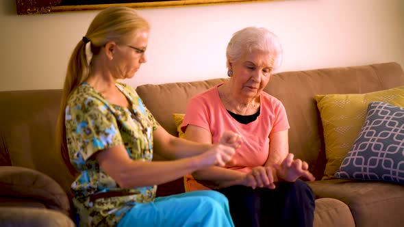 Home healthcare therapist helping elderly woman with arm stretches.