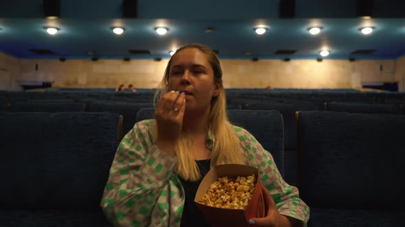 Attractive Alone Girl with Blondie Hair Eating Popcorn in Movie Theater