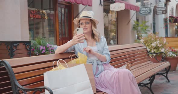 Pretty Woman Is Checking Updates on Her Smartphone, While Sitting on a Bench  