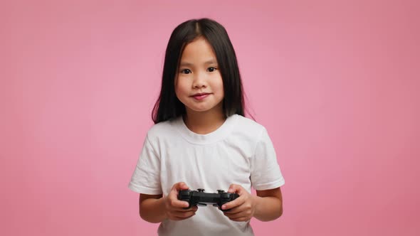 Excited Japanese Little Girl Playing Videogame Standing Over Pink Background