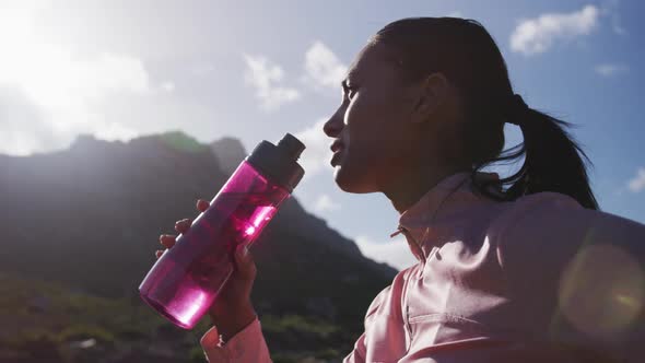 African american woman drinking water from bottle while hiking in the mountains
