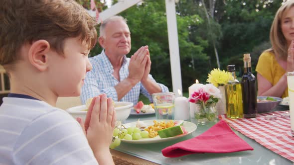 Three generation family praying before having lunch outdoors