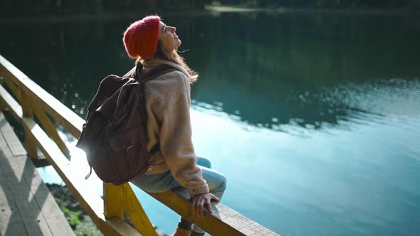 Slow Motion Inspired Joyful Woman Hiker Sits on Wooden Pier at Beautiful Mountain Lake with