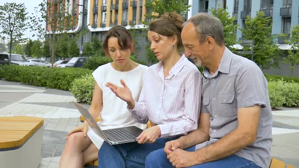 Senior Businessman and Two Female Coworkers are Discussing the Project Sitting on the Bench Near New