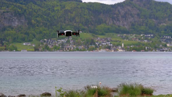 Drone with Rotating Propellers Hanging in the Air on a Background of Lake and Mountains