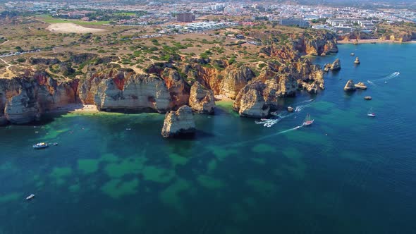 Drone shot of kayaks and boats passing in the ocean, people exploring caves and tunnels.