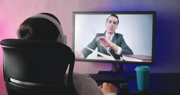 Rear View of a Young Man with Headphones Watching a Video Blog Indoors