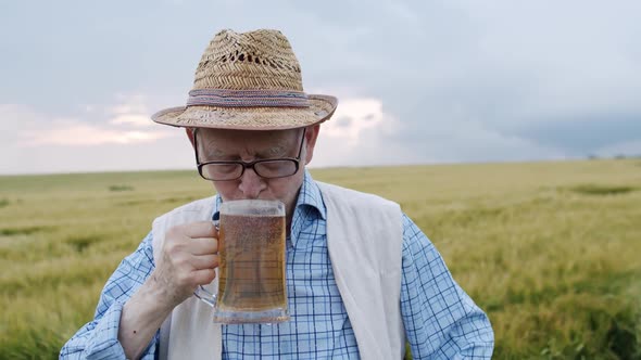 Happy Senior Drinking a Pint of Beer with Smile at Camera in Barley Field