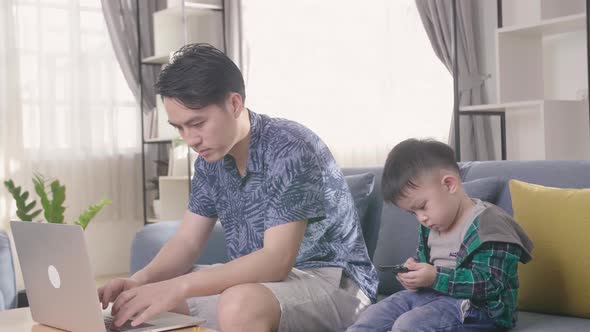 Asian Child Watching Mobile And Father Working With Laptop At Home