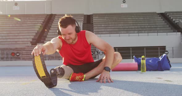 Caucasian disabled male athlete with running blade wearing headphones and stretching