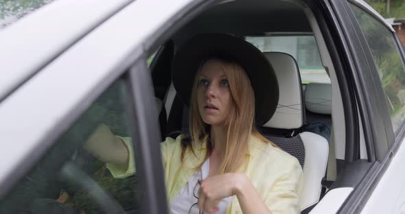 Young traveler woman sitting in car and fixing her hat in mirror.