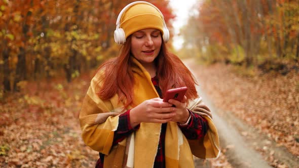 Active Caucasian Female Walking Along with Headphones Using Mobile Phone Enjoys Nature in a City