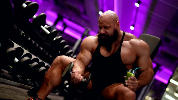 Powerlifter is Training Muscles Lifting Dumbbell and Drinking Juice with Protein in Gym