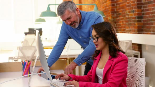 Male and female executives discussing over computer at desk