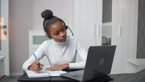 Homeschooling Online African Teen Girl Uses a Laptop and Writes at Notebook Studying By Video Call