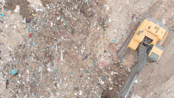 Digger clearing rubbish piled on a landfill full of trash