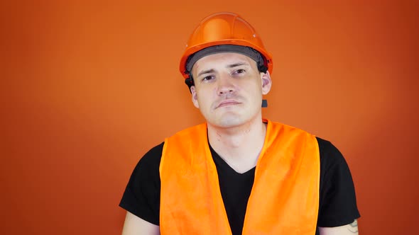 Male Construction Worker in Overalls Removing Medical Mask From Face on Orange Background