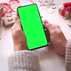 Woman holding smartphone with green screen and touch on screen on Christmas background with gifts. - VideoHive Item for Sale