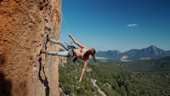 Strong and Muscular Fit Rock Climber Hangs on Rope on Vertical Cliff