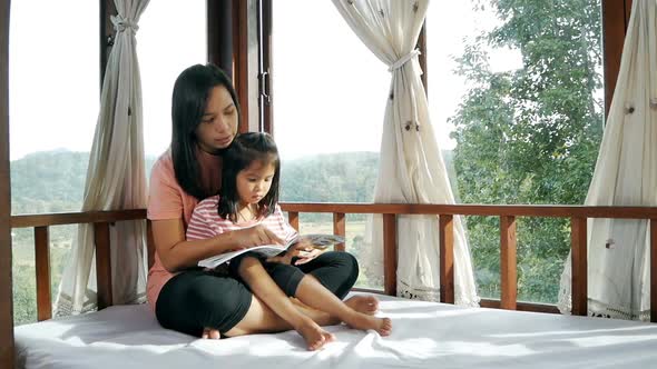 Closeup of mother and daughter reading a book on the bed.