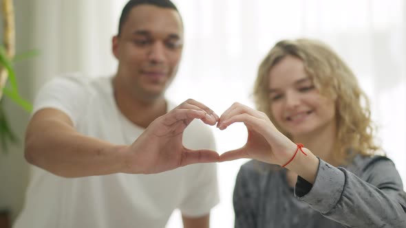 Closeup Hands of Young Interracial Loving Happy Couple Making Heart Shape with Blurred Smiling