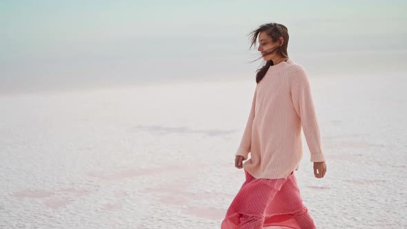 Walking Girl in Big Sweater and Blowing Pink Dress at Beautiful Landscape of Salt Flats at Pink Lake