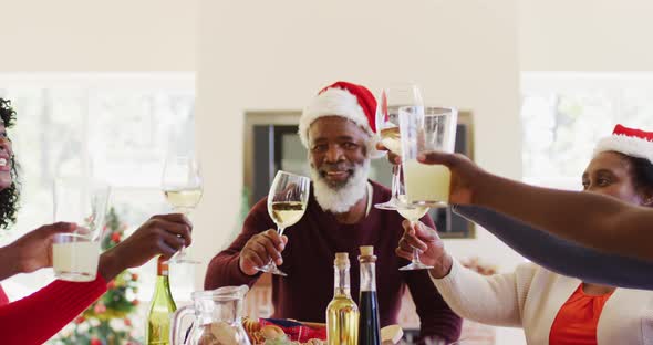 African american family in santa hats toasting while sitting on dining table having lunch together a