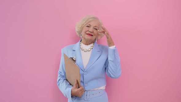 Cute Business Woman in a Formal Suit Adjusts Her Hair on an Isolated Pink Background