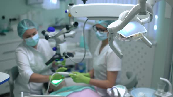 Closeup Dental Lamp with Blurred Orthodontist and Assistant Using Microscope at Background Curing