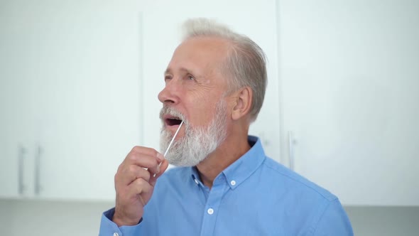 Closeup of Mature Caucasian Adult Man Taking Swab Sample of Mouth Carrying Out Coronavirus Self Home