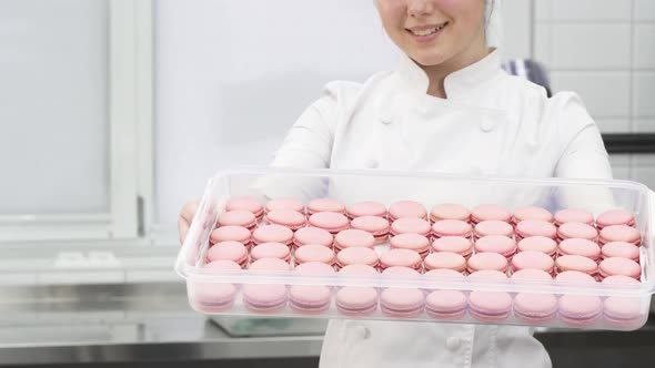 Cropped Shot of a Pastry Chef Smiling Holding Out Tray with Pink Macaroons