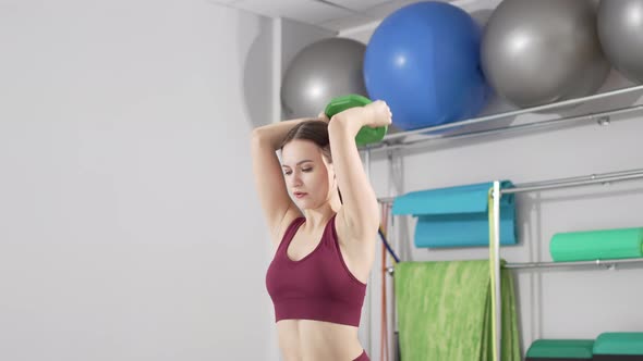 a Beautiful and Slender Young Woman Does Exercises with Weights in the Gym