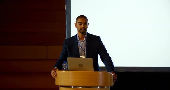 Young mixed-race male speaker with laptop speaking on stage in auditorium 4k