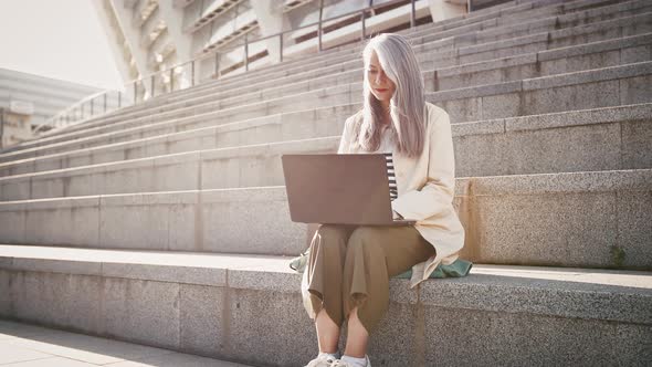 Asian Middleaged Female in Casual Outfit is Working Online on Laptop Computer While Sitting on