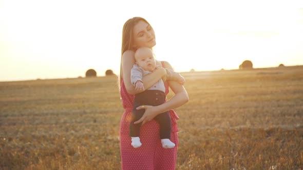 Happy Mother Caresses Her Baby Son with Harmony in Hay Field During Sunset