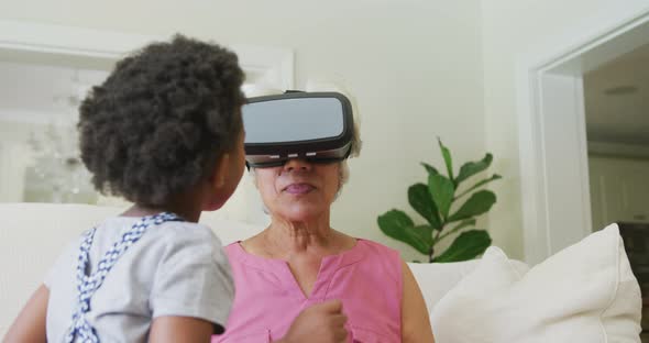 Happy african american grandmother using vr headset with granddaughter in living room